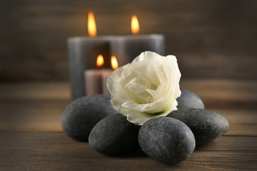 Alight wax grey candle with pebbles and beautiful flower on wooden background