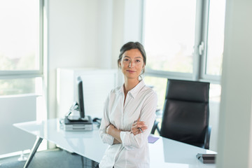 business woman leaning against her glass desk, luminous office
