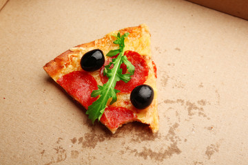 Bitten slice of pepperoni pizza with olives and arugula on cardboard