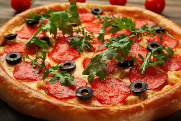 Tasty pizza with salami decorated with tomatoes on wooden background, close up