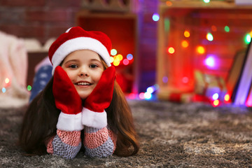 Fototapeta na wymiar Pretty little girl in red hat and gloves laying in Christmas decorated room