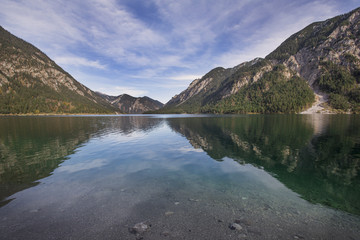 Die Bergketten der Tiroler Alpen spiegeln sich auf der glatten Oberfläche des Plansees in Österreich.
