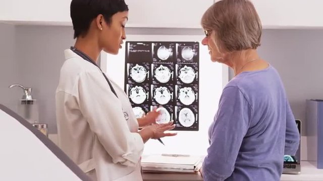 Young female doctor reviewing x-ray scans with elderly woman
