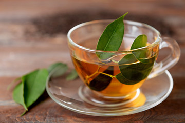 Glass cup of tea with green leaves on wooden background