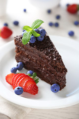 Chocolate cake with chocolate cream and fresh berries on plate, on light background