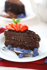 Chocolate cake with chocolate cream and fresh berries on plate, on wooden table, on light background