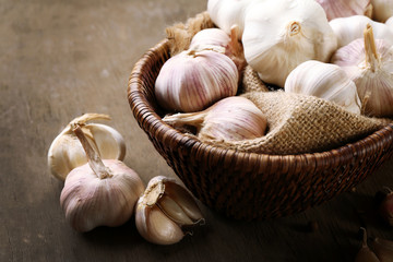 Garlic in wicker bowl on wooden background, close up