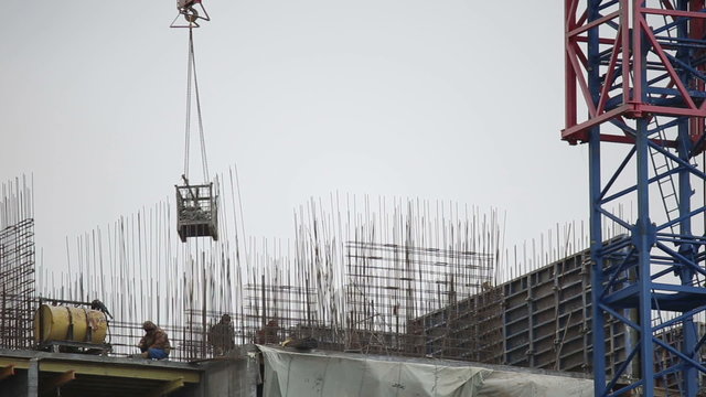 Construction crane and builders working on a construct of a multystoried house
