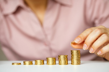 Female hand stacking gold coins into increasing columns