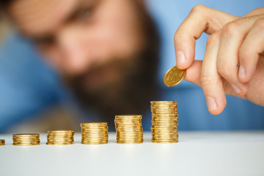 Beared man stacking gold coins into increasing columns