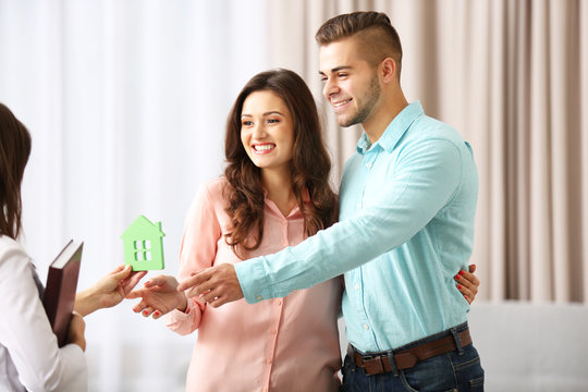 Estate agent giving model of house to  couple, on light background