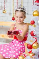 Fototapeta premium Four-year girl stretches forward a little gift sitting snowy Christmas trees