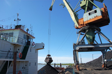 Fototapeta premium Dockside cargo crane loads coal at river port Kolyma