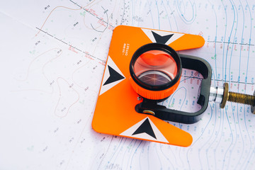 orange theodolite prism lies on a background geodetic maps of the area