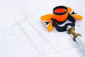orange theodolite prism lies on a background geodetic maps of the area - obrazy, fototapety, plakaty