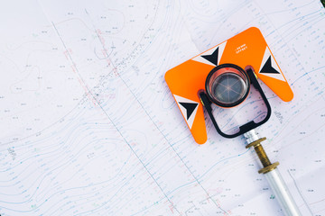 orange theodolite prism lies on a background geodetic maps of the area