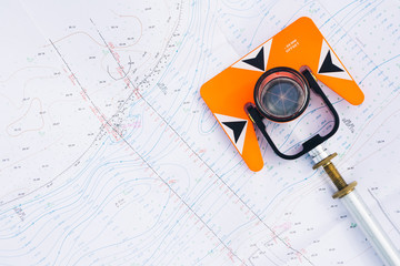 orange theodolite prism lies on a background geodetic maps of the area - obrazy, fototapety, plakaty