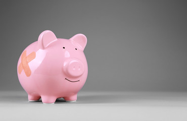 Piggy Bank with adhesive bandage on grey background