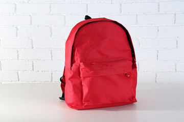 School backpack on wooden table, on wall background