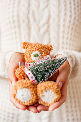 Woman in white knitted sweater holding toy bear with christmas ribbon and fir tree.