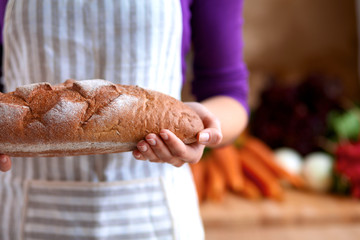 Young woman holding tasty fresh bread in her kitchen