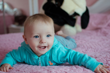 Cute smiling baby lying on tummy in parent's bed with a big toy dog on background. 