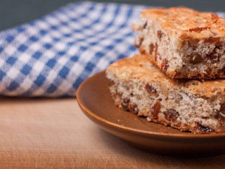 Closeup view of two piece of biscuit cake with walnuts and raisins on brown ceramic saucer, with blue plaid cloth on the background.