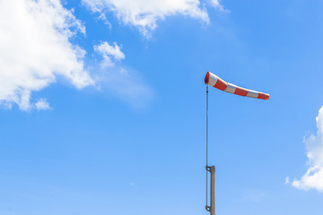 Red and white windsock blows against a blue sky