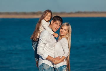 Fototapeta na wymiar Young family in blue jeans hugging on the background of water