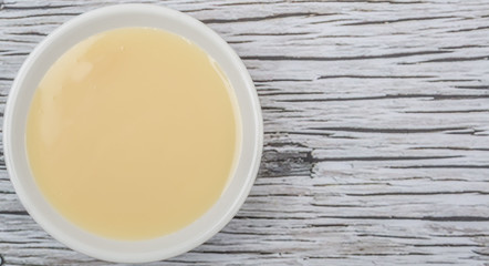 Fototapeta na wymiar Sweet condensed milk in white bowl over wooden background