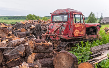 Fototapeta na wymiar Red bulldozer stands near firewood heap against cloudy sky background 