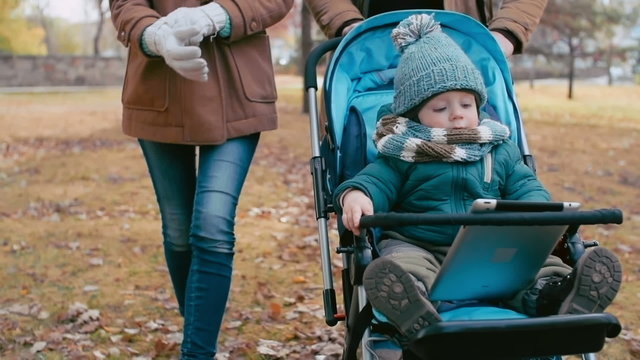 Baby boy sitting in pram and playing or watching cartoons on tablet computer during a walk with his parents 