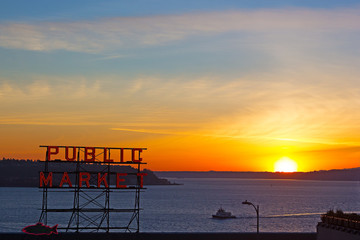 Spectacular sunset over Puget Sound photographed from the Pike Public Market in Seattle, Washington, USA. Winter sunset, water, mountains on horizon and Public Market neon sign.