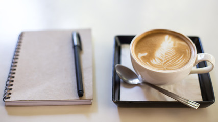 Hot latte art coffee cup on wooden table and note book