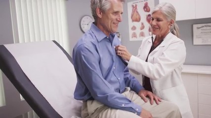 Middle-aged male patient sitting in hospital room with senior doctor checking his vitals - Powered by Adobe