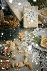 Obraz na płótnie Canvas Christmas still life with present, almond, cinnamon, snowflakes on wooden table. Top view.