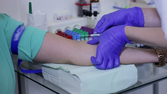 Doctor Drawing Blood Sample From Arm In Red Tube