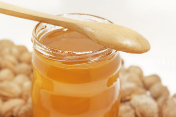 Jar of honey and spoon with walnuts on white