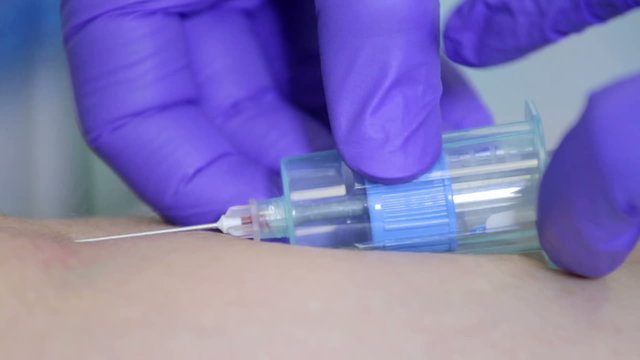 Doctor drawing blood sample from arm in blue tube