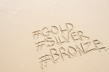 Hashtag social media message for gold, silver, and bronze medals, sport's first, second, and third place, written in sand on the beach in Rio de Janeiro, Brazil