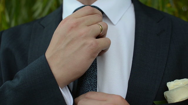 Man in suit adjusts his tie in the park . Close-up
