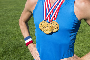 Athlete wearing chocolate chip cookies gold medals standing in front of green grass playing field...