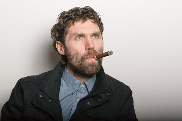 bearded man against a white wall smoking a cigar