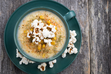 corn soup with popcorn in cup on wooden table, top view