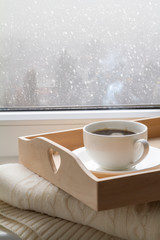 Coffee on tray and sweater in from of snowing winter