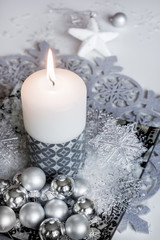 White burning candle with a monochrome christmas ornaments setup