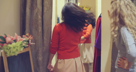 Pretty lady trying on new skirt and sweater in dressing room to show her outfit to her friend but she is already exhausted from shopping