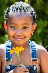 Cute african girl holding orange flower outdoors.