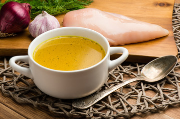 Chicken bouillon in the white bowl on the rustic wooden background.
