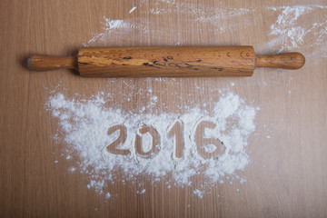 Figures 2016 on flour spilling on wooden background. Selective f
